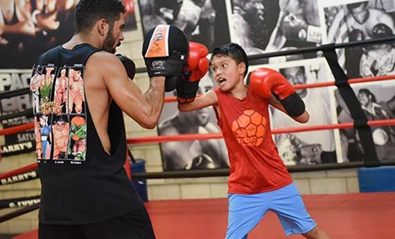 A coach holds pads for a young boxer at Barry's Boxing Center